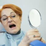 woman at dentist examines her teeth in mirror